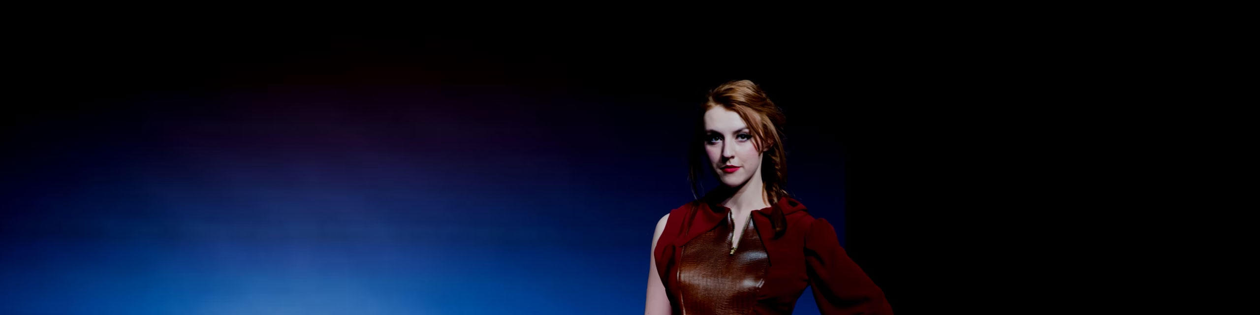 Female model in burgundy outfit in front of navy blue background.
