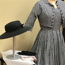 A historic dress, gloves and hat on a display.